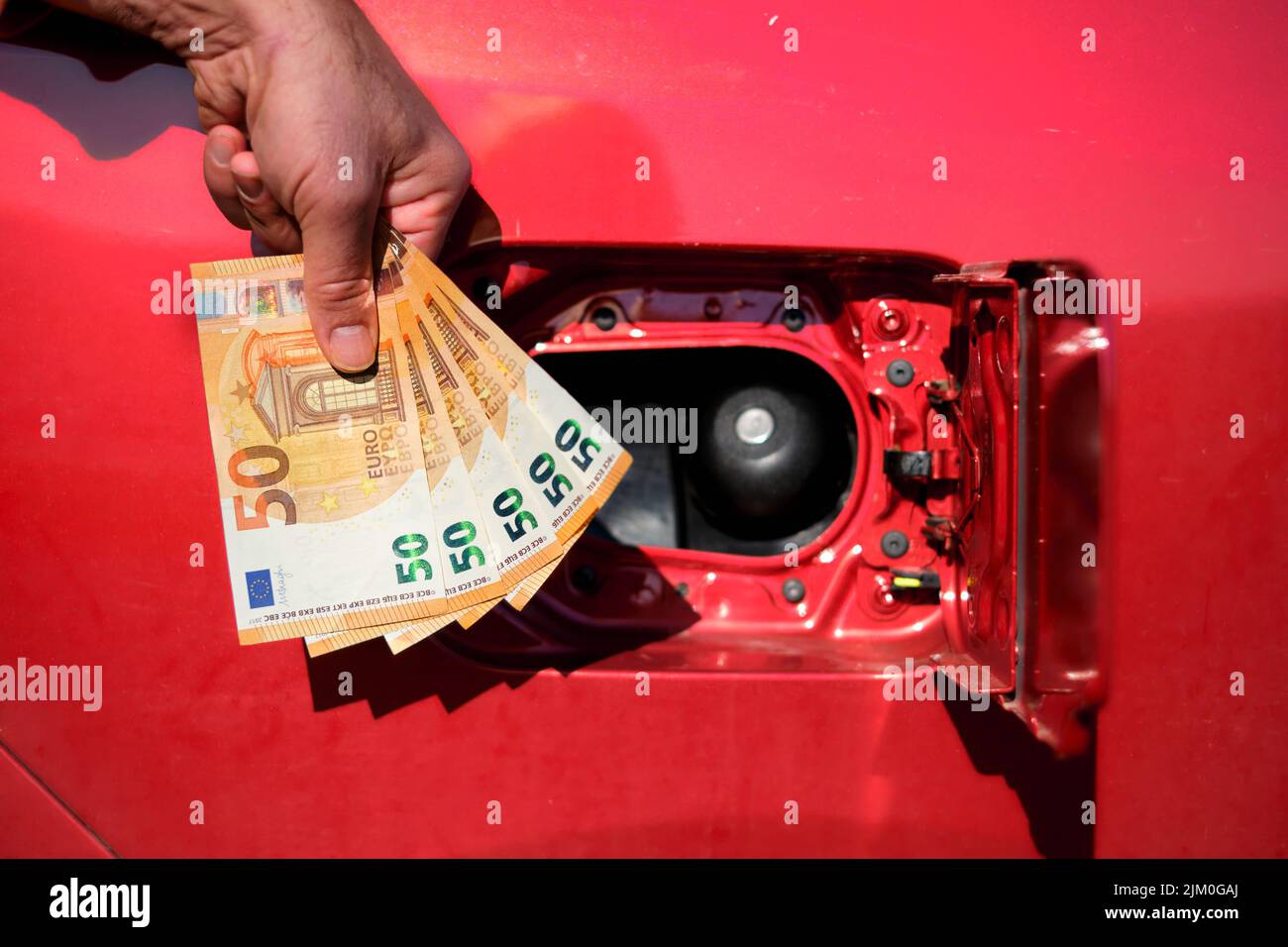 Une main tenant plusieurs cinquante billets d'euros à côté du réservoir de carburant d'une voiture, symbolisant l'augmentation des coûts de carburant et de transport. Banque D'Images