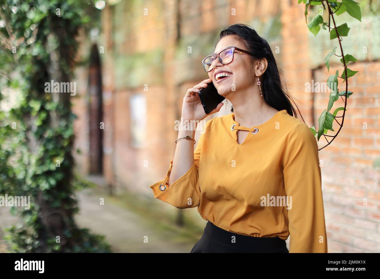 Une jeune brunette latino-américaine parle au téléphone en portant des lunettes souriantes Banque D'Images