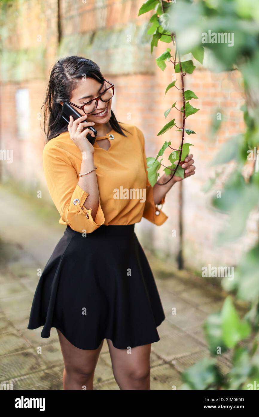 Jeune brunette latino-américaine, femme parlant au téléphone touchant l'usine Banque D'Images