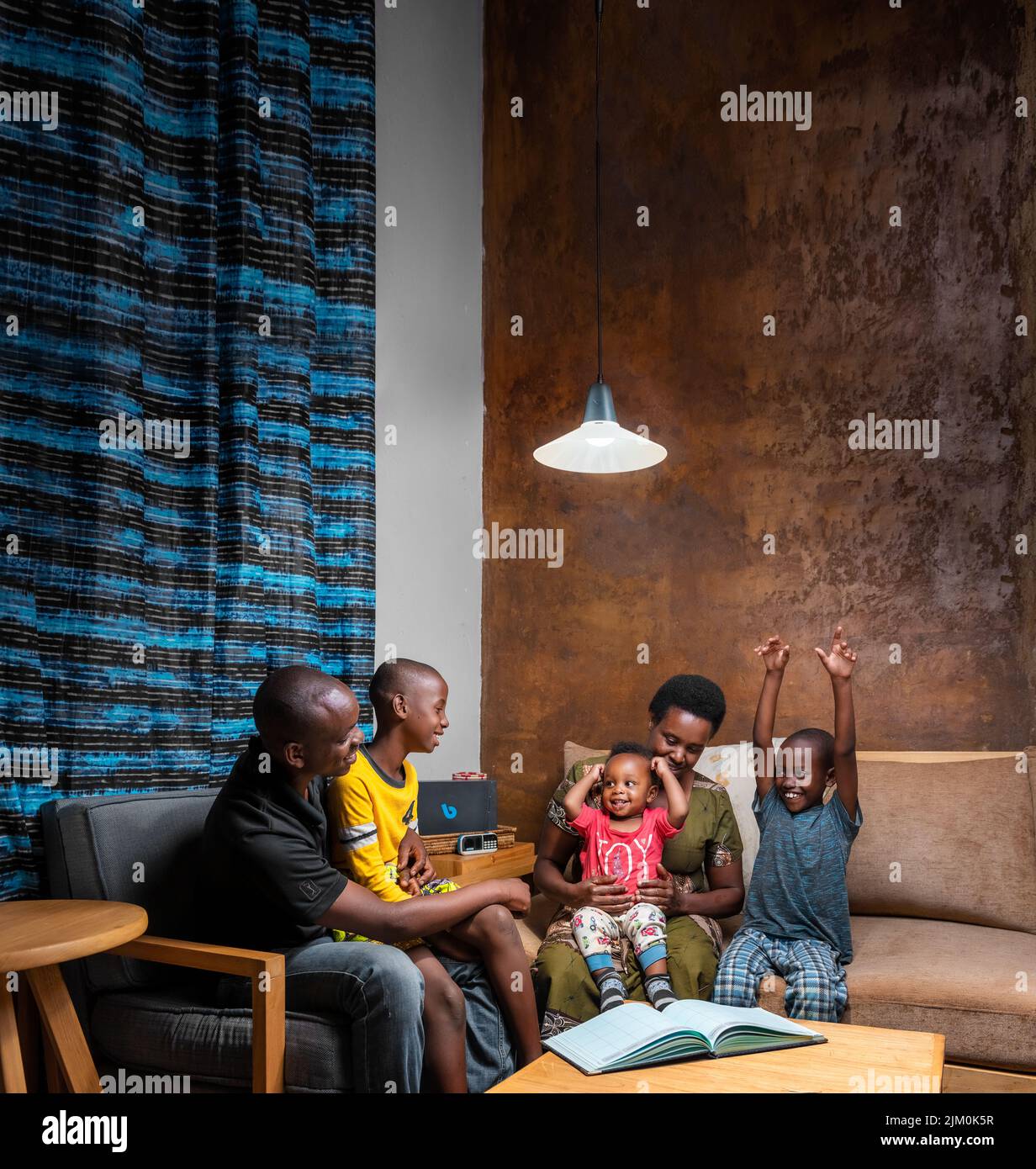 Une famille rwandaise assise dans le salon souriant et s'amusant en lisant un livre Banque D'Images