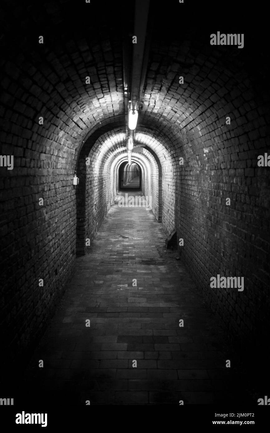 Photo verticale noir et blanc d'un tunnel souterrain en briques avec lumières. Banque D'Images