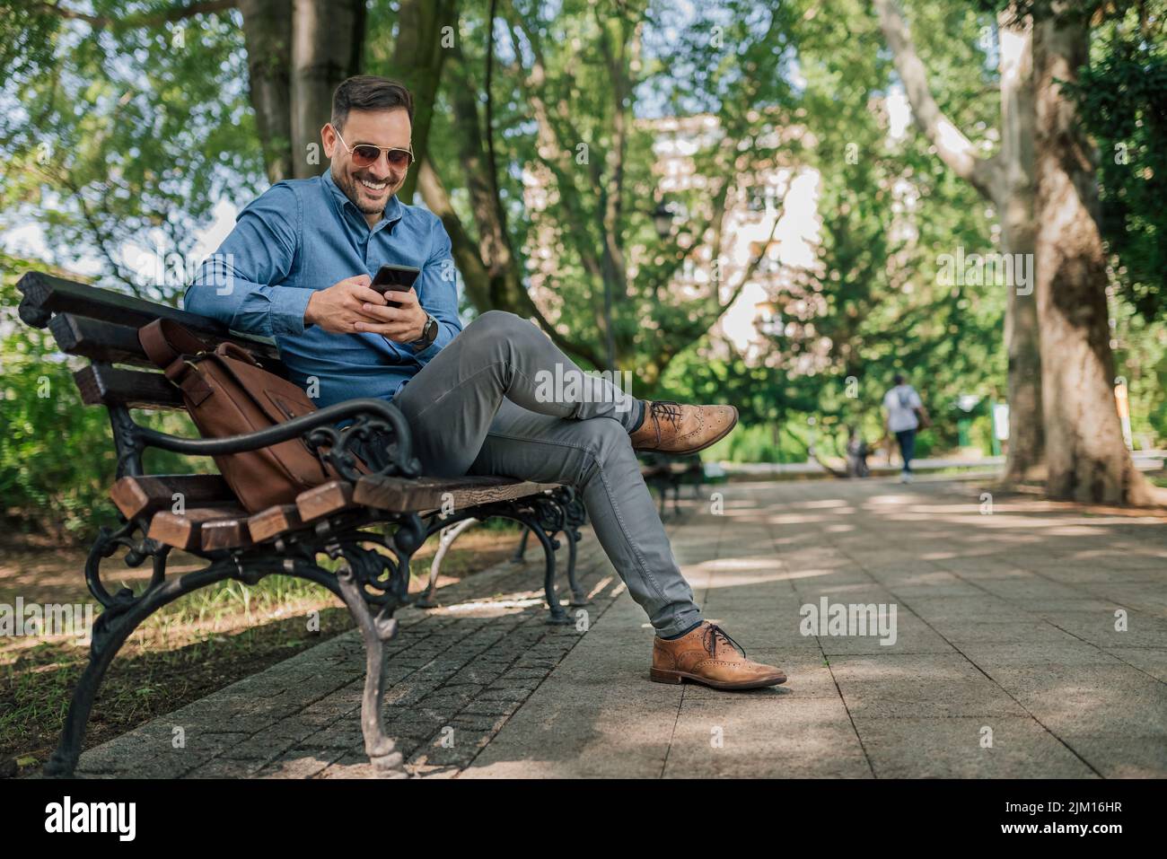 Messagerie texte homme d'affaires souriant sur smartphone. Un jeune homme professionnel confiant est en réseau tout en étant assis sur le banc. Il porte des coffrages à la TH Banque D'Images