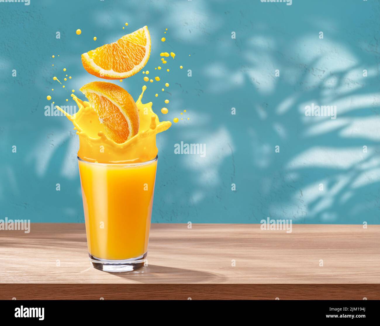 Verre de jus d'orange avec éclaboussures d'orange sur la table et mur en stuc avec ombres à feuilles à l'arrière-plan. Banque D'Images