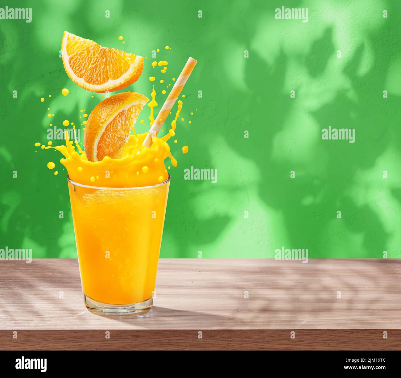 Verre de jus d'orange avec éclaboussures d'orange sur la table et mur en stuc avec ombres à feuilles à l'arrière-plan. Banque D'Images