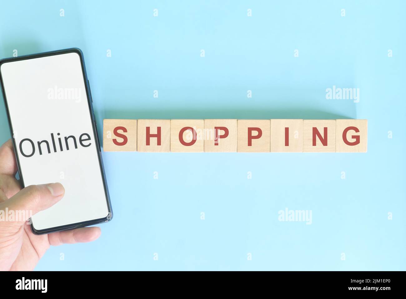 Concept d'achat en ligne. Main tenant le téléphone portable à côté de blocs de bois sur fond bleu. Banque D'Images