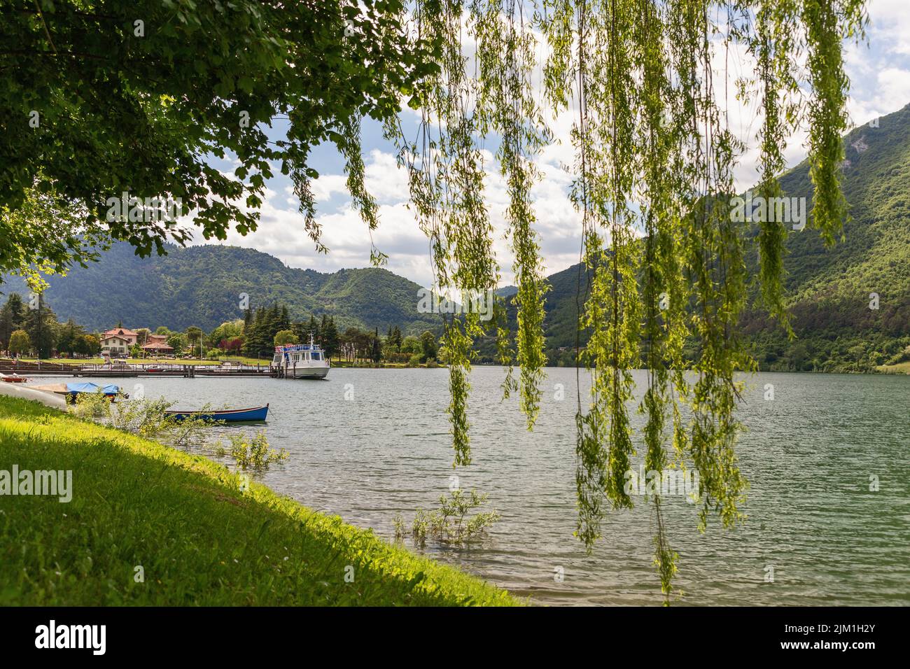 Vue sur le lac alpin Idro (Lago d'Idro) entouré de longues branches de saules vertes s'étendant vers l'eau. Brescia, Italie Banque D'Images