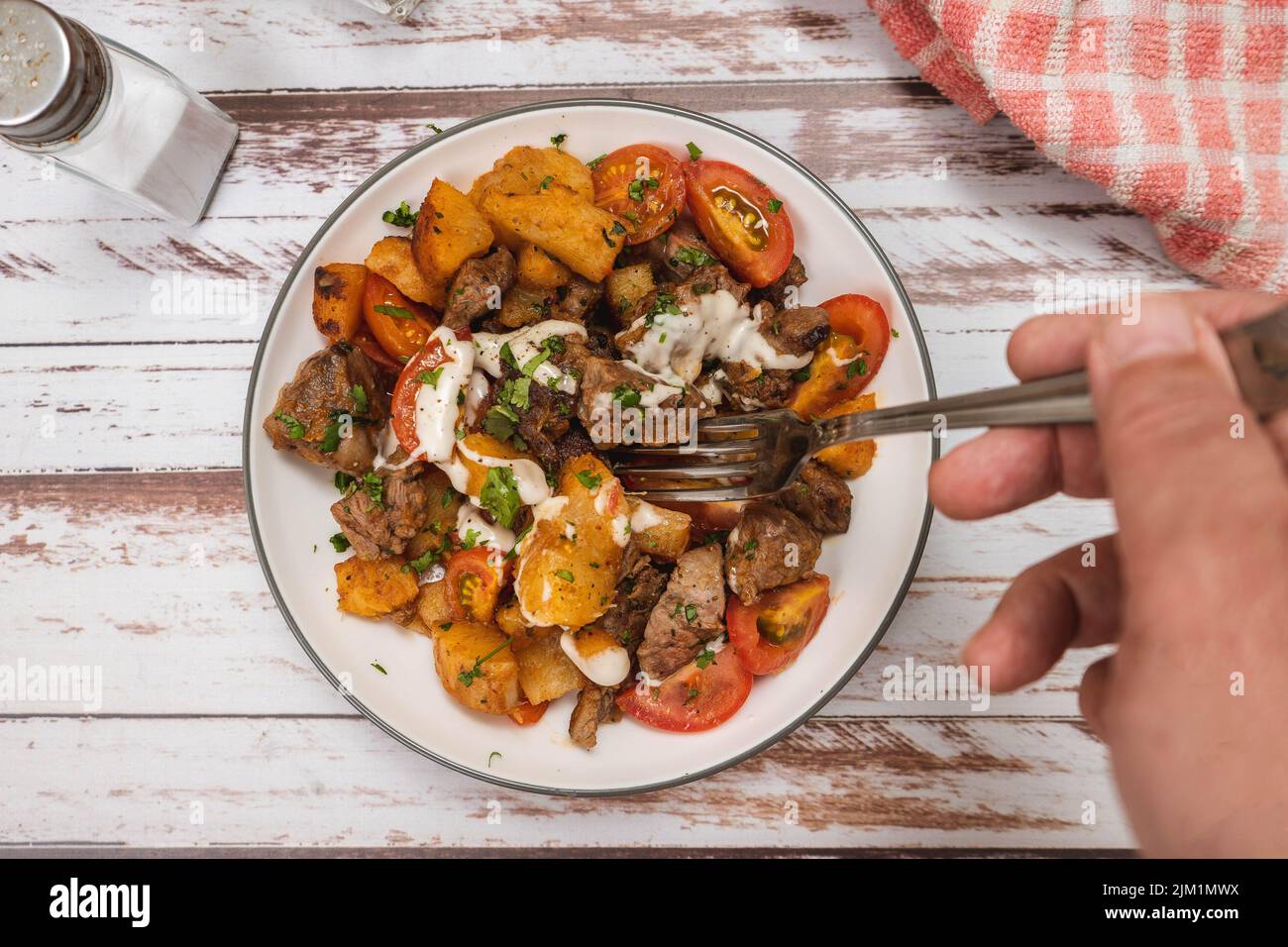 Prendre à la main une portion de morceaux de bœuf sautés avec du manioc ou du manioc, de la ciboulette, du poivre, du citron et de la tomate cerise sur une surface rustique. Vue de dessus Banque D'Images