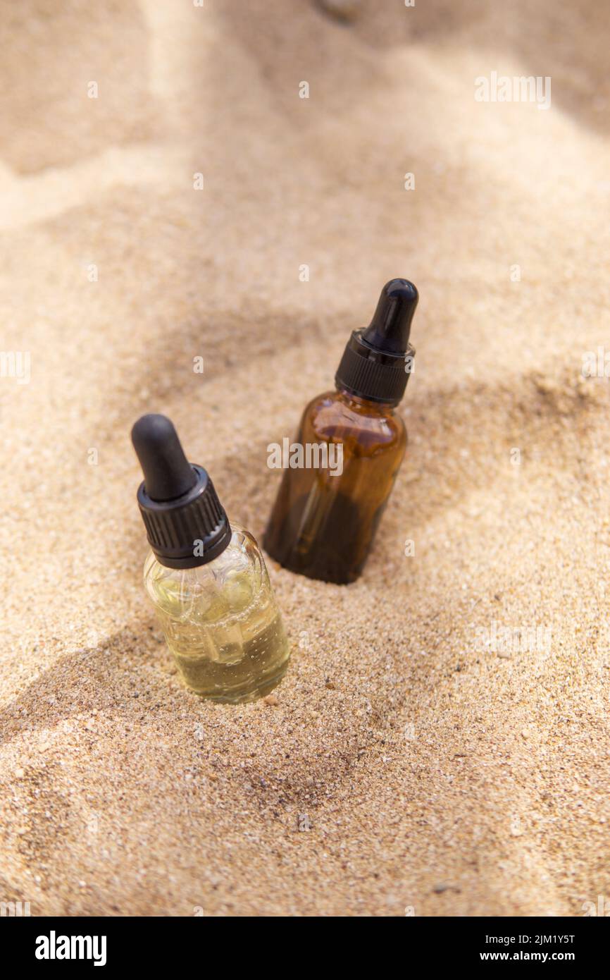 Sérum cosmétique dans une bouteille en verre avec une pipette dans le sable Banque D'Images