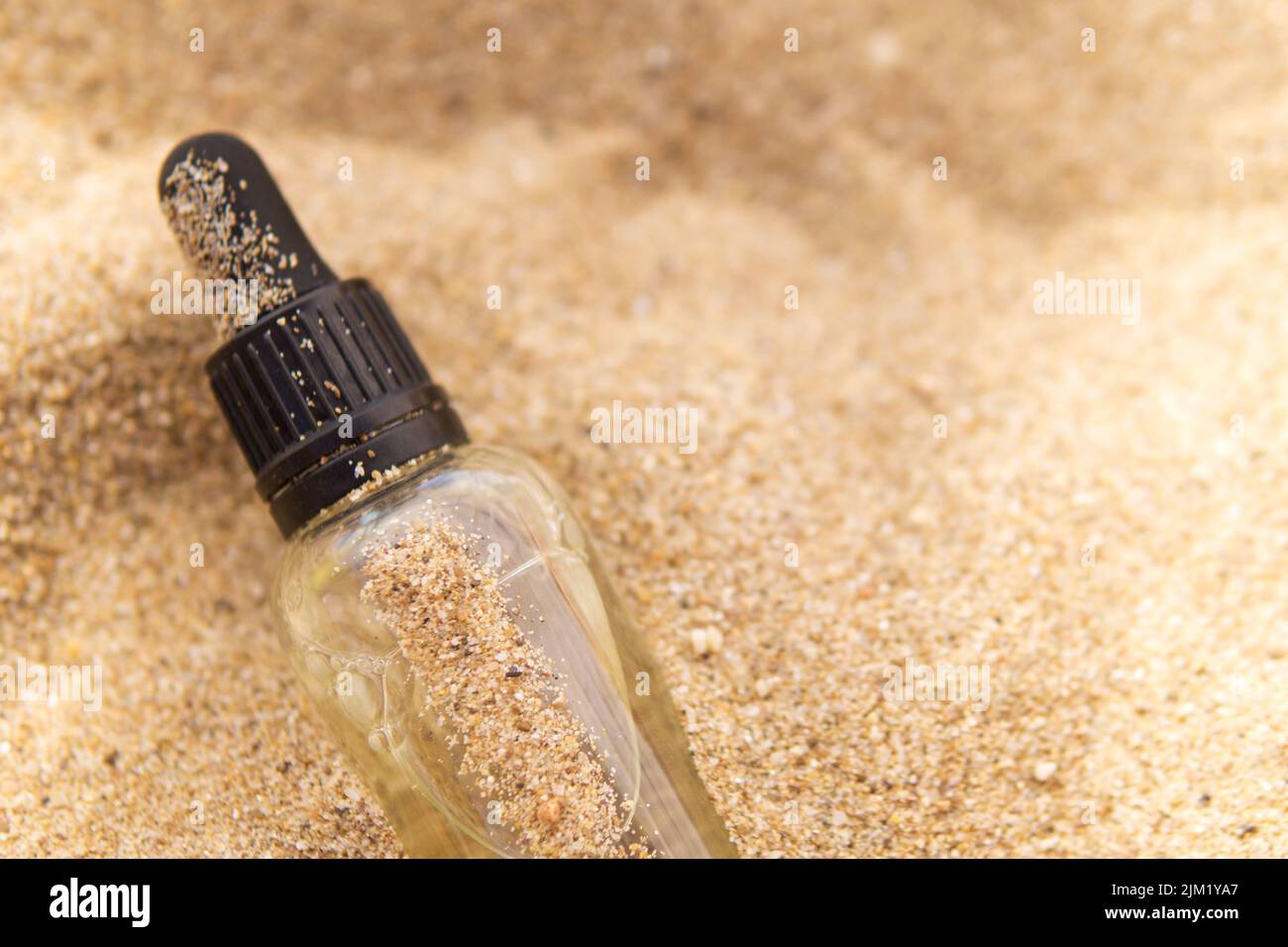 Sérum cosmétique dans une bouteille en verre avec une pipette dans le sable Banque D'Images