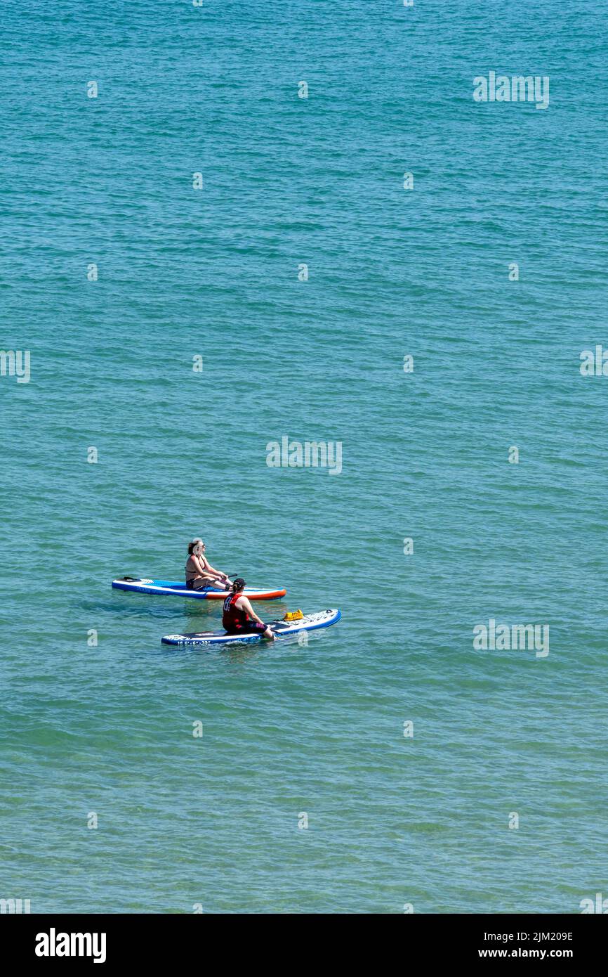 Les vacanciers assis sur leurs paddleboards Stand Up flottant dans la mer à Newquay Bay, en Cornouailles, en Angleterre, au Royaume-Uni. Banque D'Images