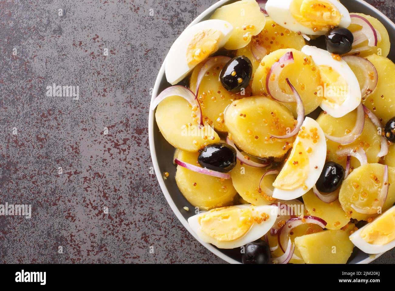 Salade de pommes de terre orientale roumaine aux oignons, aux olives et aux œufs bouillis sur une assiette sur la table. Vue horizontale du dessus Banque D'Images