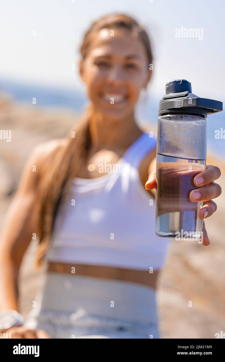 Femme souriante tenant une bouteille d'eau après avoir fait de l'exercice à l'extérieur Banque D'Images