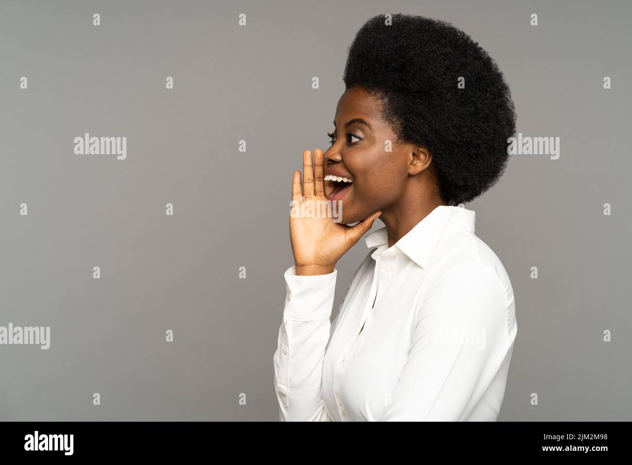 Une femme afro-américaine aux cheveux bouclés dit du texte publicitaire dans un espace vide sur fond gris Banque D'Images
