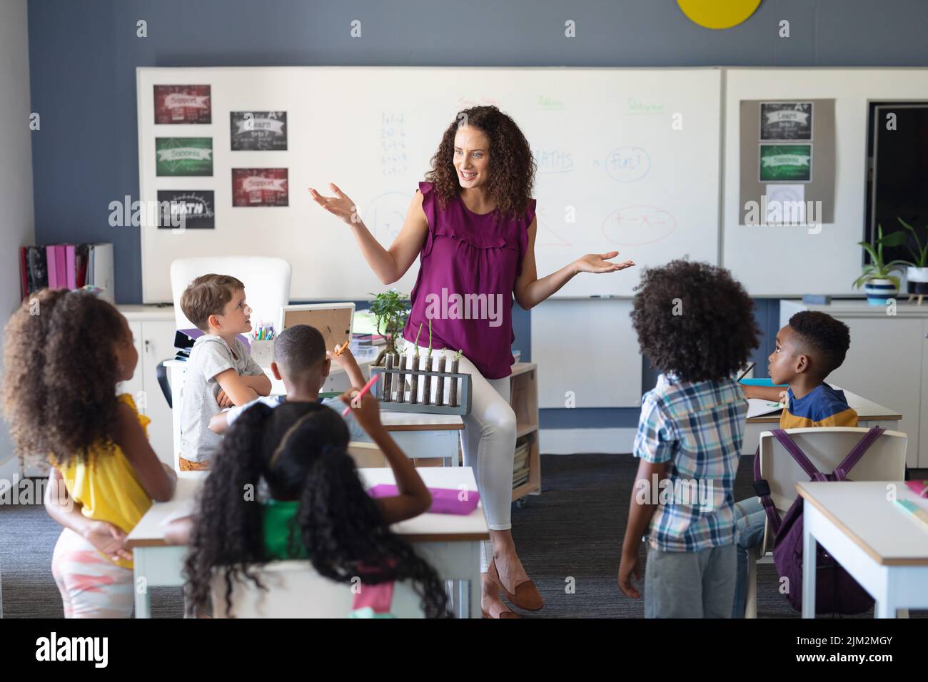 Élèves élémentaires multiraciaux qui regardent une jeune enseignante de race blanche pendant un cours de sciences Banque D'Images