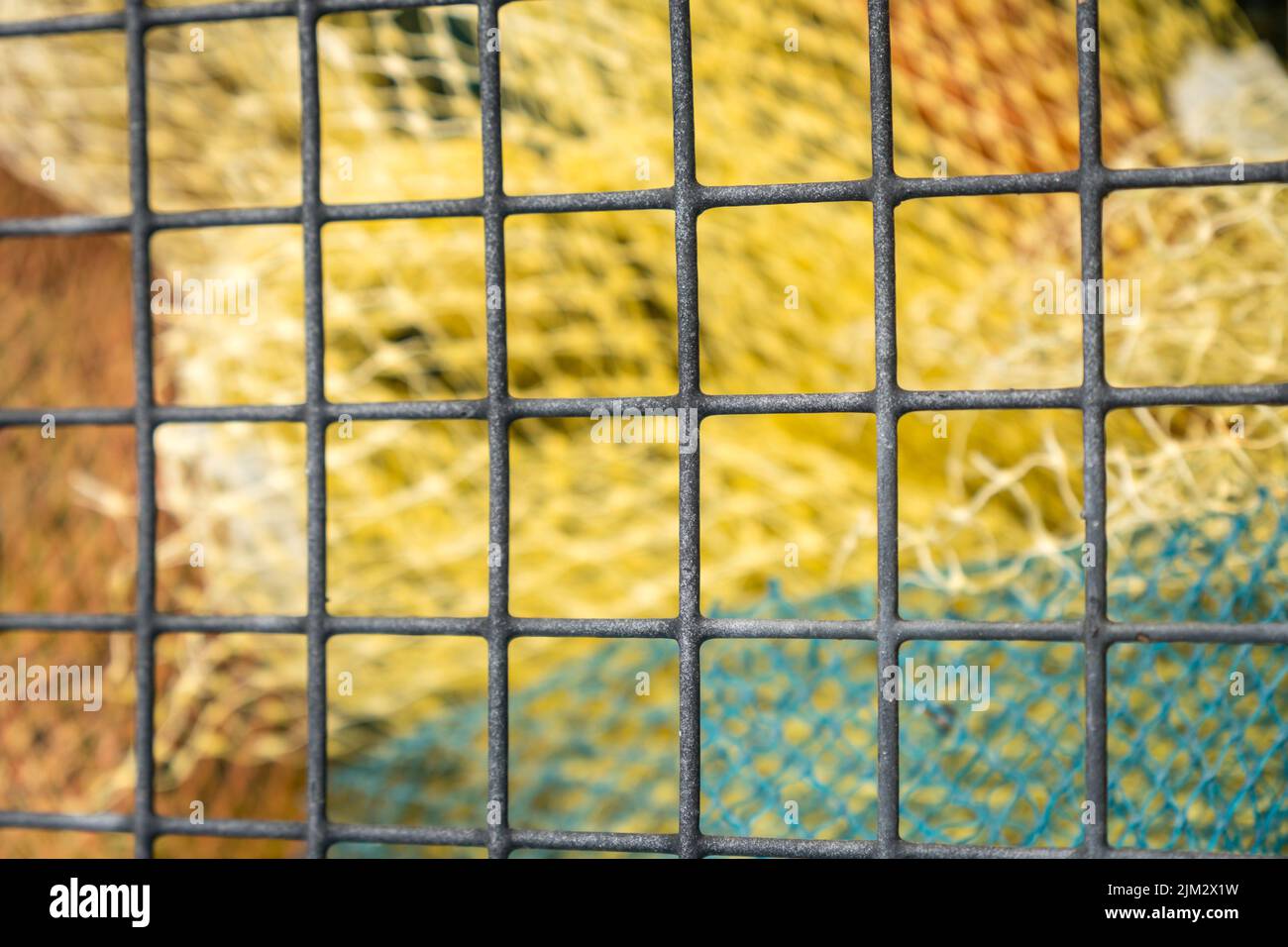 Vue abstraite des filets de pêche colorés à travers la clôture. Mise au point sélective intentionnelle et bokeh d'arrière-plan. Banque D'Images