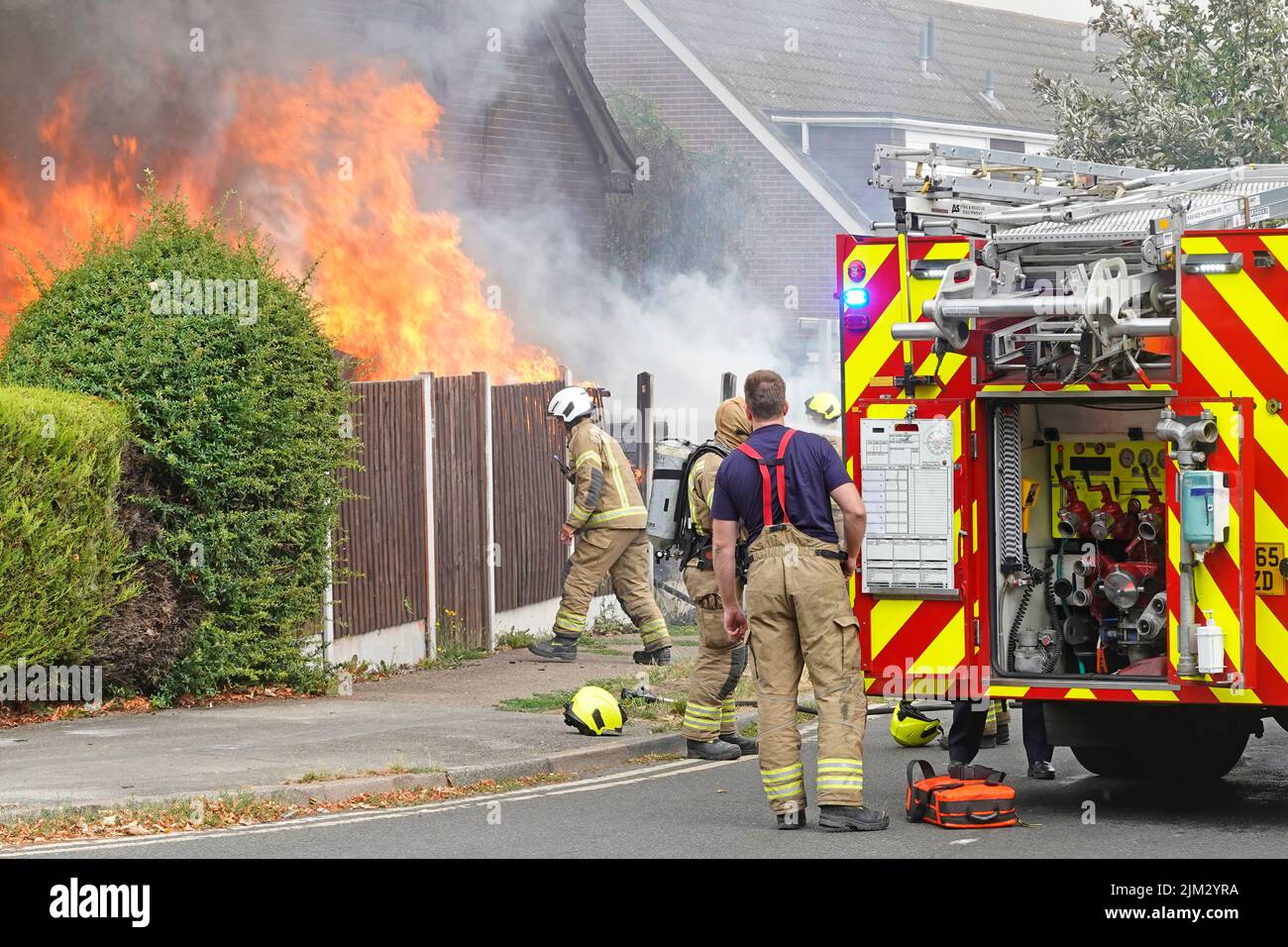 Feu moteur tendre vient d'arriver vue arrière portes ouvertes à la pompe à eau soupapes de commande pompiers travaillant sur maison feu flammes scène de rue Essex Angleterre Royaume-Uni Banque D'Images