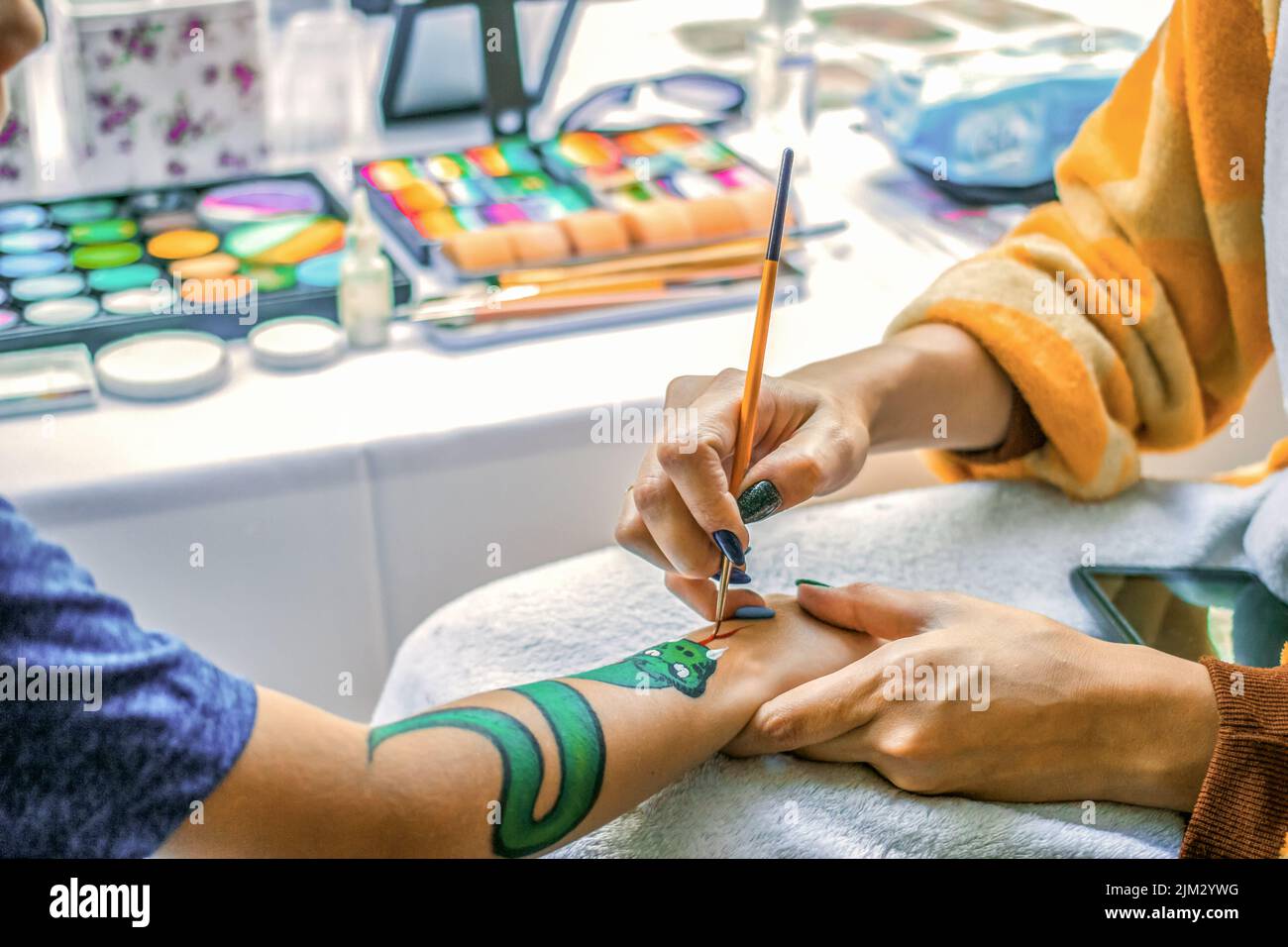 Jeune fille artiste dessine un dragon sur la main de l'enfant. Peindre la peau avec des peintures, gros plan, sans visage. Banque D'Images