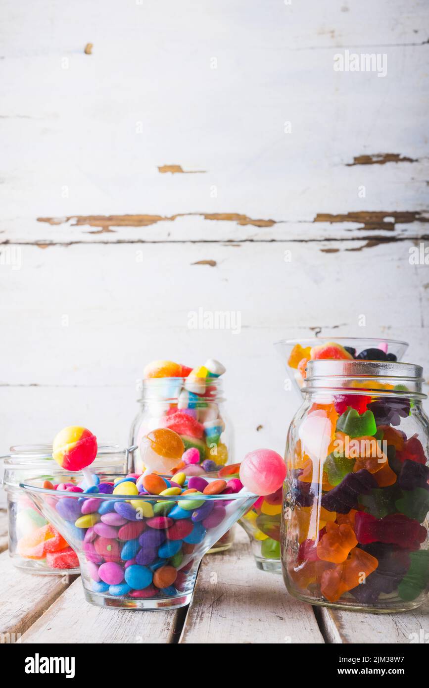Gros plan de plusieurs bonbons et sucettes multicolores dans des pots en verre et un bol sur la table Banque D'Images