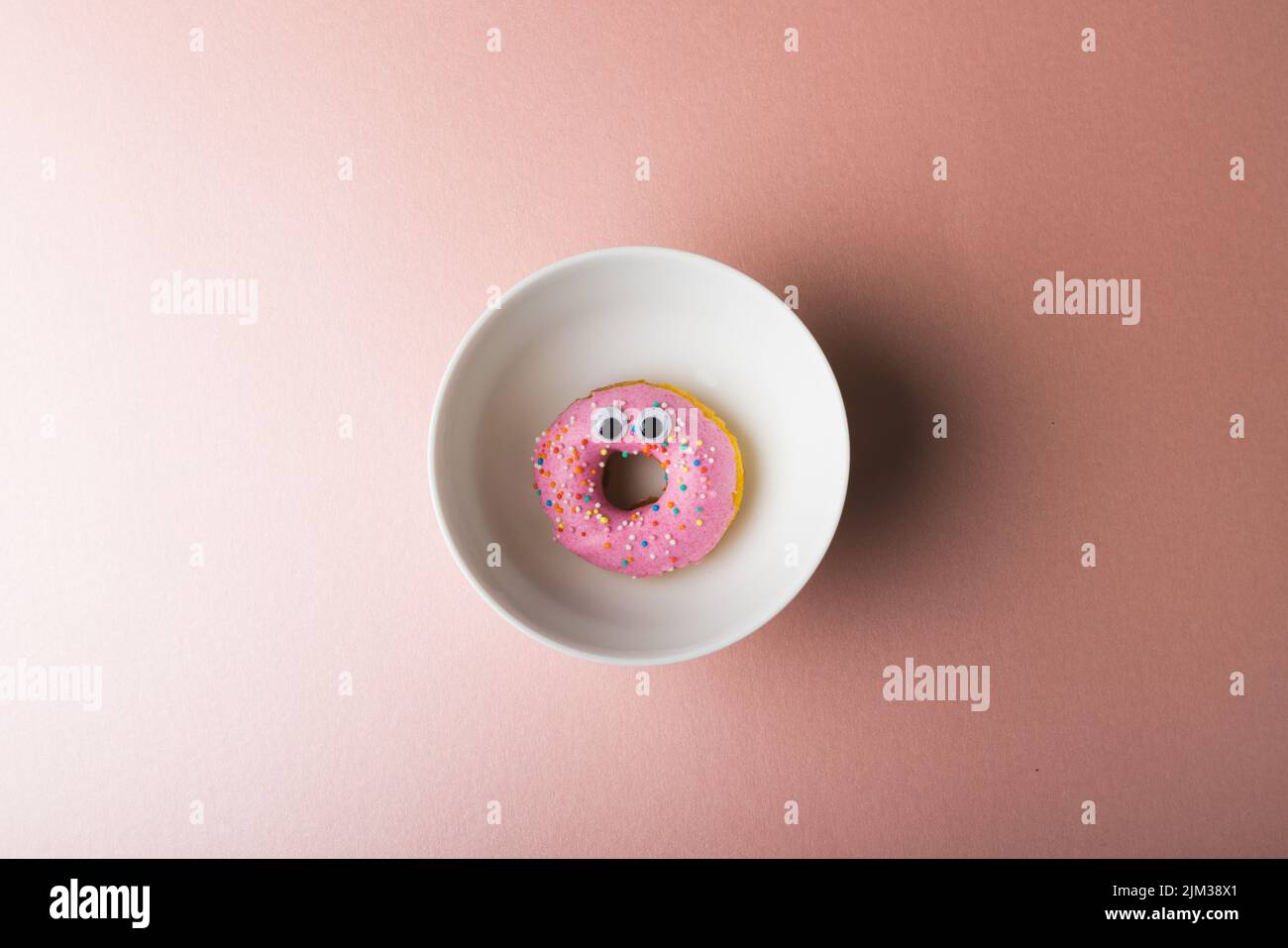 Directement au-dessus de la vue du donut rose avec des yeux de bonne taille dans la plaque autour de l'espace de copie sur fond coloré Banque D'Images