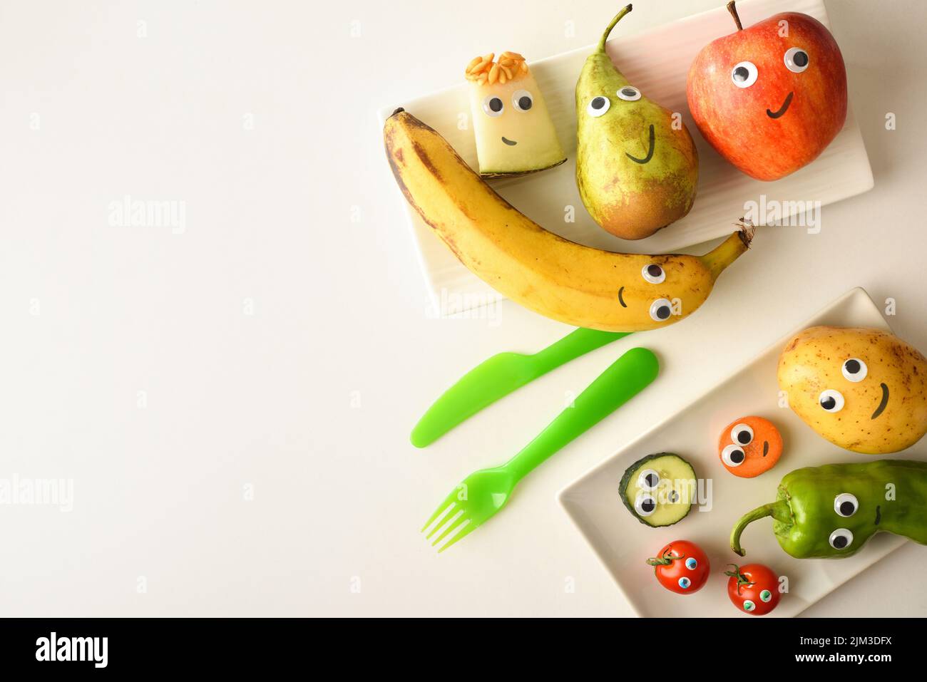 Fond avec assiette de fruits drôles avec yeux et bouches dessinés servi pour les enfants sur table blanche. Vue de dessus. Banque D'Images