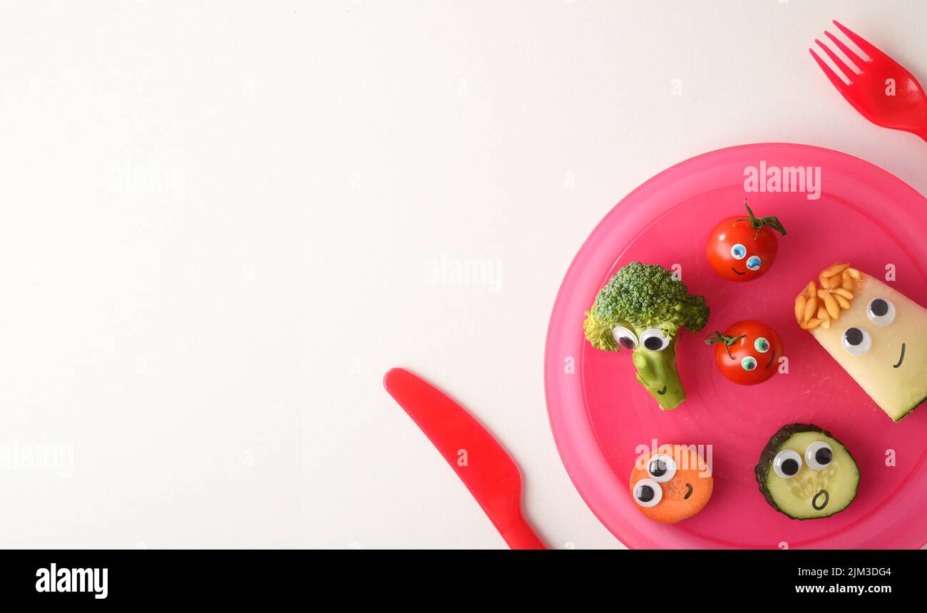Filet de sécurité avec une jolie assiette de fruits et légumes amusants servis pour les enfants avec des couverts rouges pour les enfants sur une table blanche. Vue de dessus. Banque D'Images