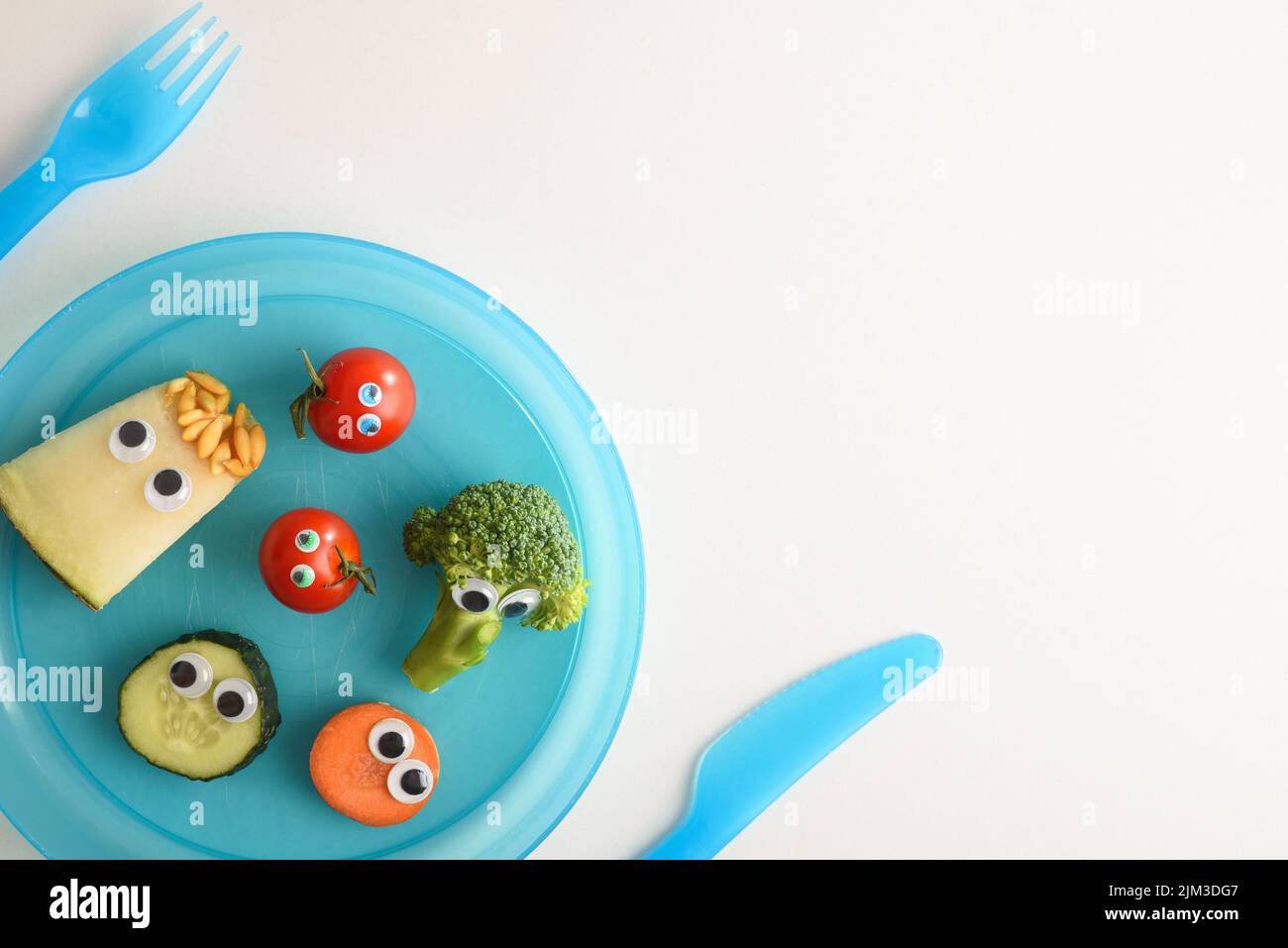 Filet de sécurité avec une jolie assiette de fruits et légumes amusants servis pour les enfants avec des couverts bleus pour les enfants sur une table blanche. Vue de dessus. Banque D'Images