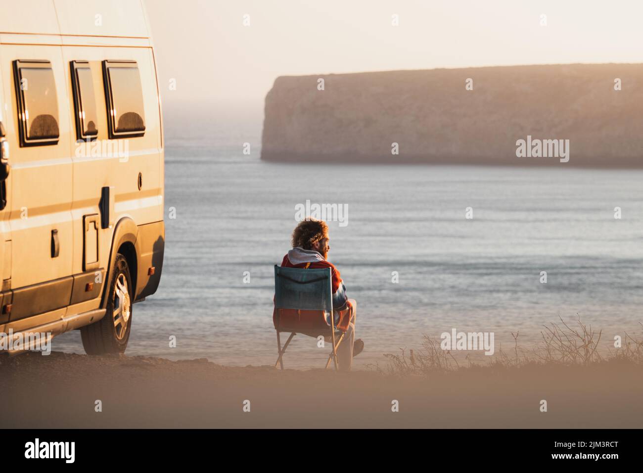 Une personne assise sur une chaise sur la rive à côté d'un camion et regardant la mer Banque D'Images