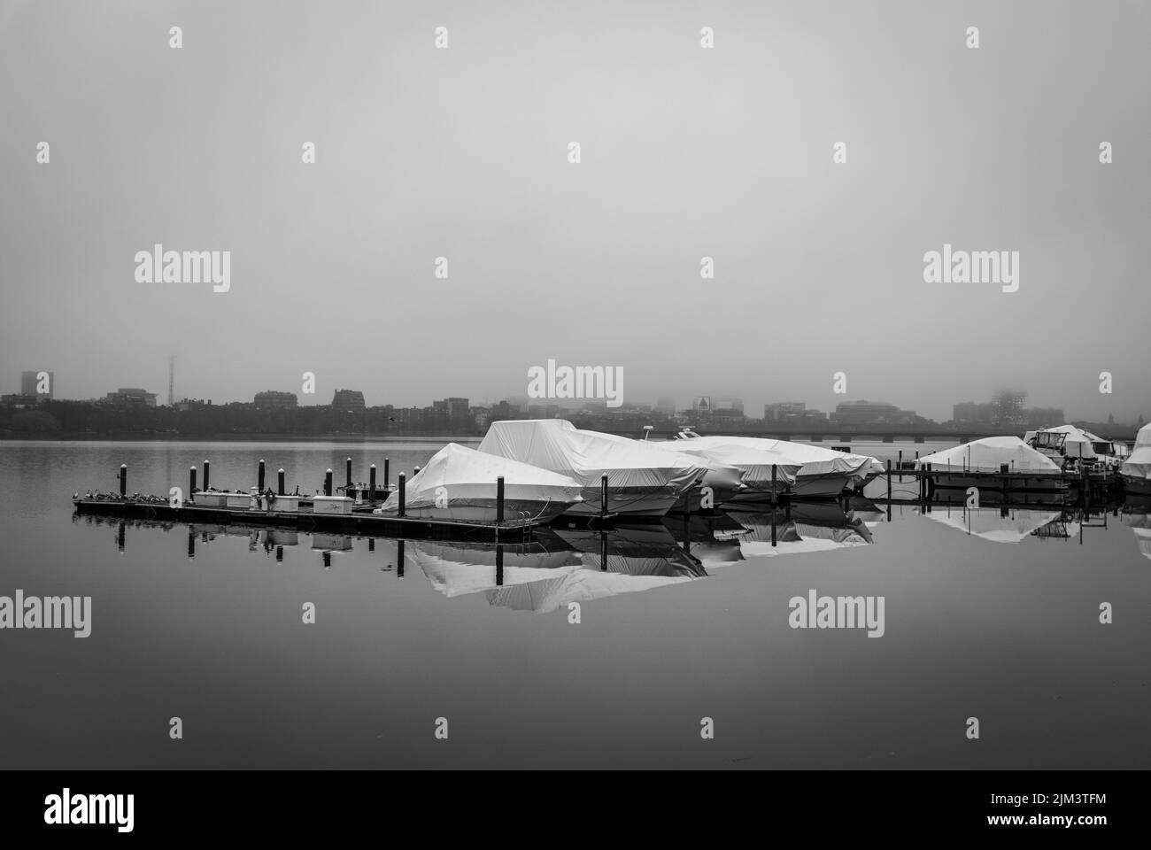 Une photo en niveaux de gris des bateaux garés dans le stockage d'hiver se reflétant sur l'eau à la lumière du jour avec le ciel gris en arrière-plan Banque D'Images