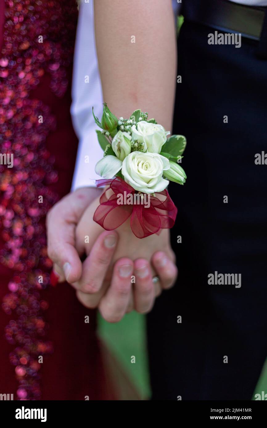 Gros plan d'un jeune couple tenant les mains avec une fleur de fleur au poignet en relief avec un arrière-plan flou Banque D'Images