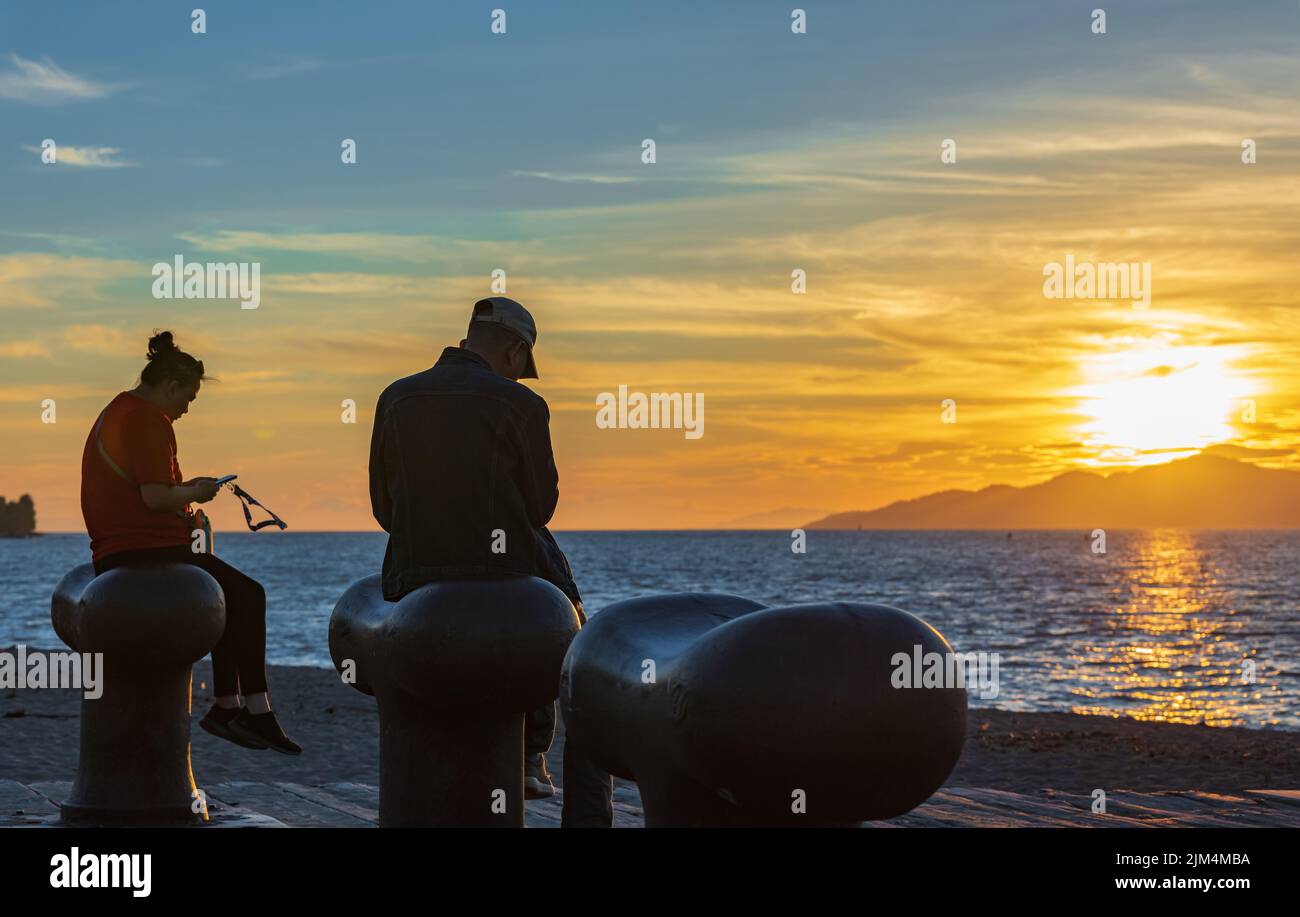 Vue de la silhouette d'une personne à l'aide d'un smartphone au coucher du soleil. Femme et homme utilisant des téléphones intelligents assis sur la plage à Sunset-24 juillet,2022-Vancouver C.-B. C Banque D'Images