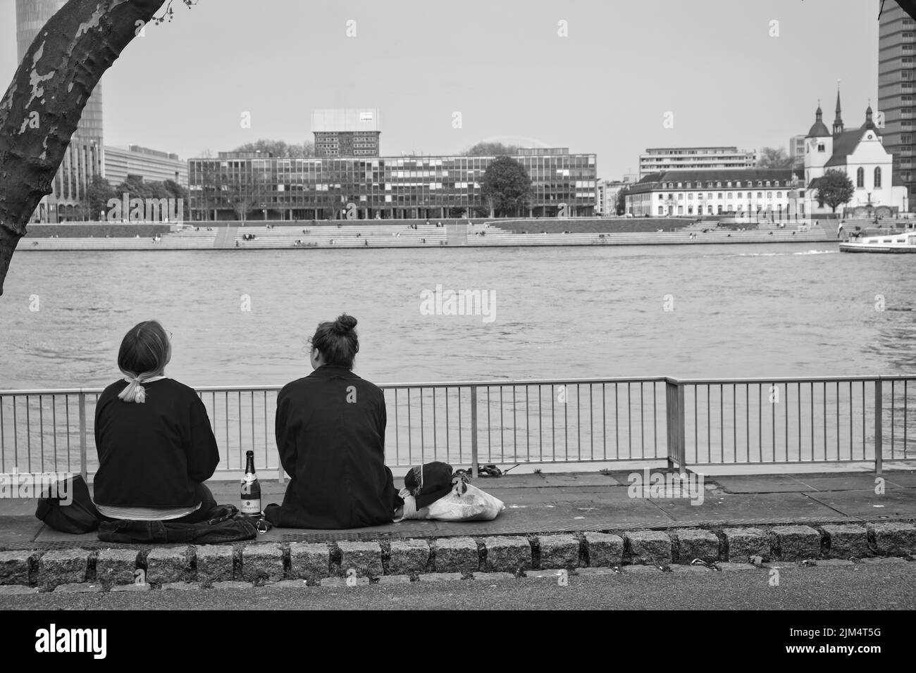 deux jeunes femmes sont assises sur un mur sur les rives du rhin à cologne avec une bouteille de vin mousseux le beau jour de printemps, pure joie de vivre Banque D'Images