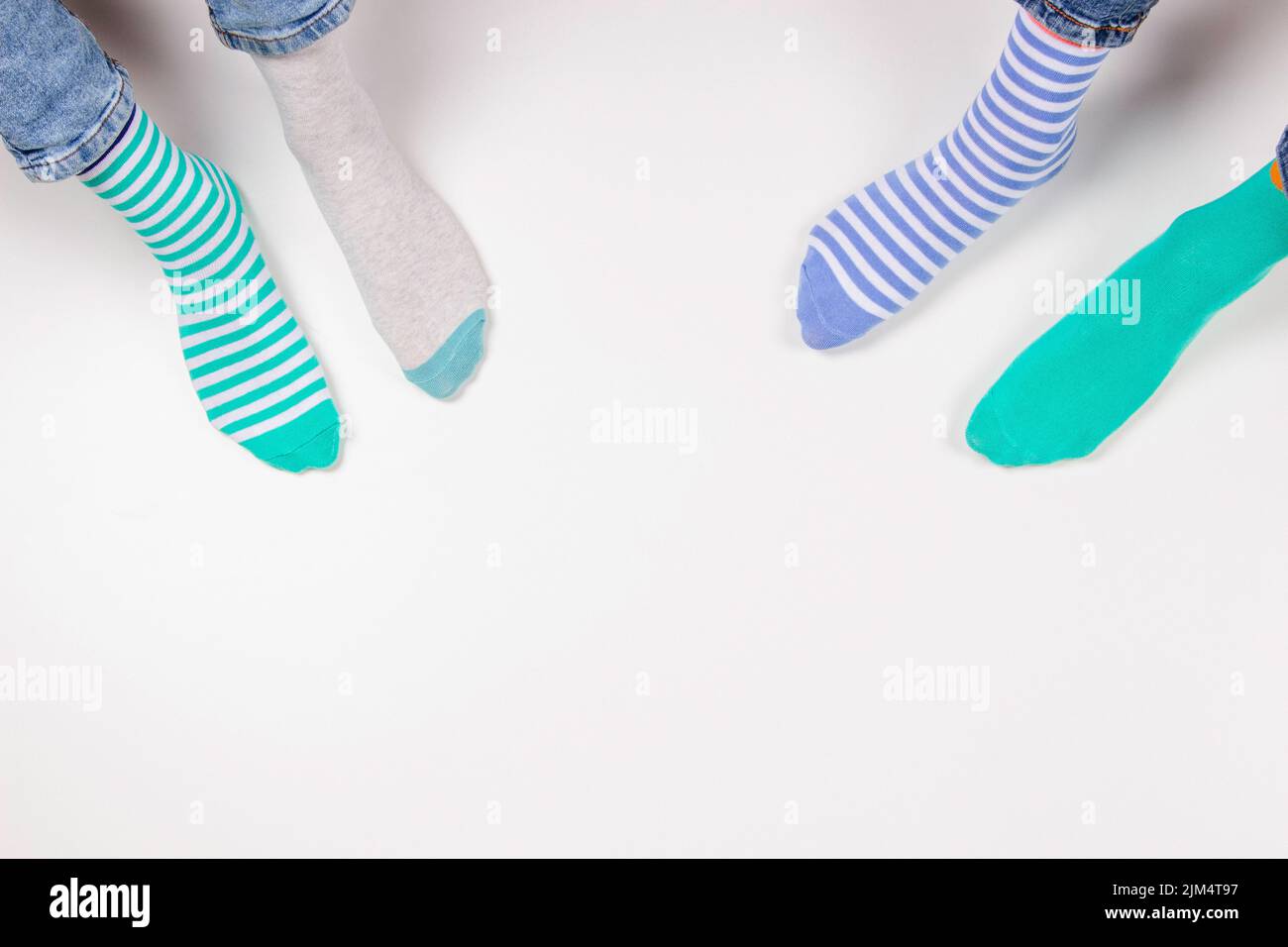 Enfant portant différentes paires de chaussettes. Pieds d'enfant dans des chaussettes mal assorties assis sur fond blanc. Journée des chaussettes impaires, semaine anti-intimidation, syndrome de Down Banque D'Images