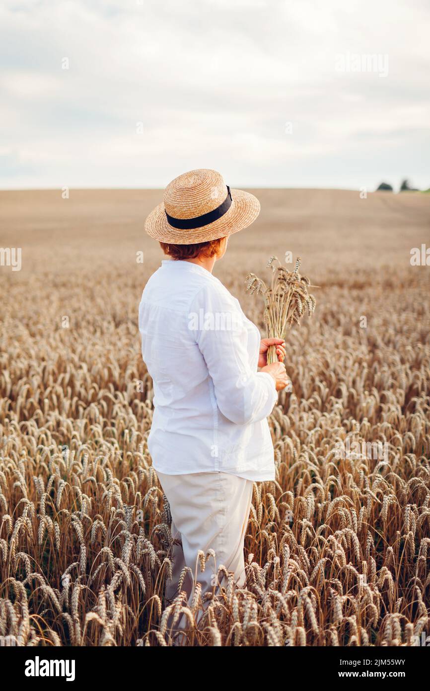 Femme paysanne vérifiant le blé dans le champ d'été au coucher du soleil holding bouquet. Récolte en Ukraine. Agriculture et agriculture. Symbole ukrainien Banque D'Images