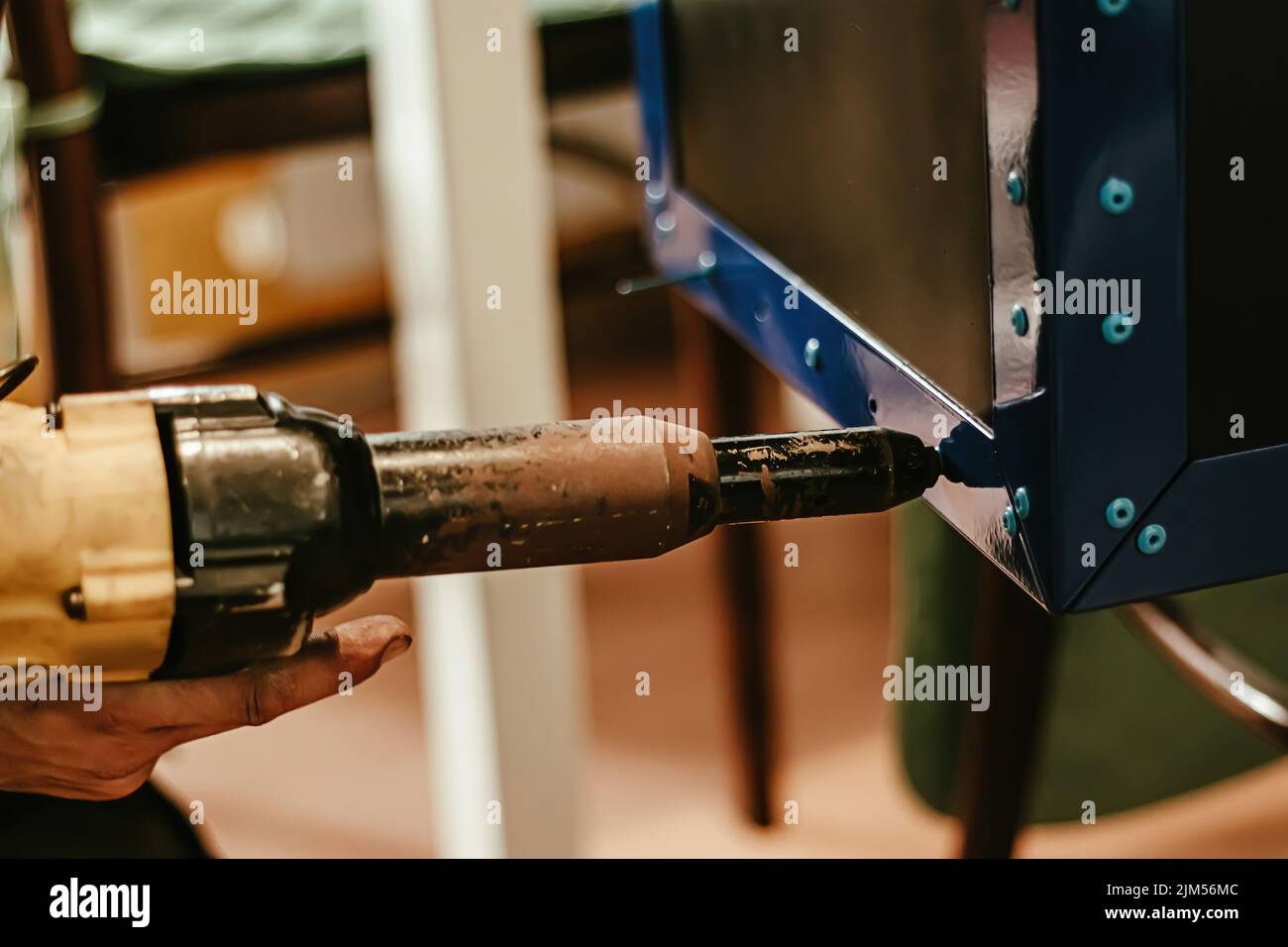 Le travailleur masculin utilise un pistolet à riveter électrique. Machine à riveter à main et pose des rivets. Atelier de travail de charpentier ou mécanicien. Banque D'Images