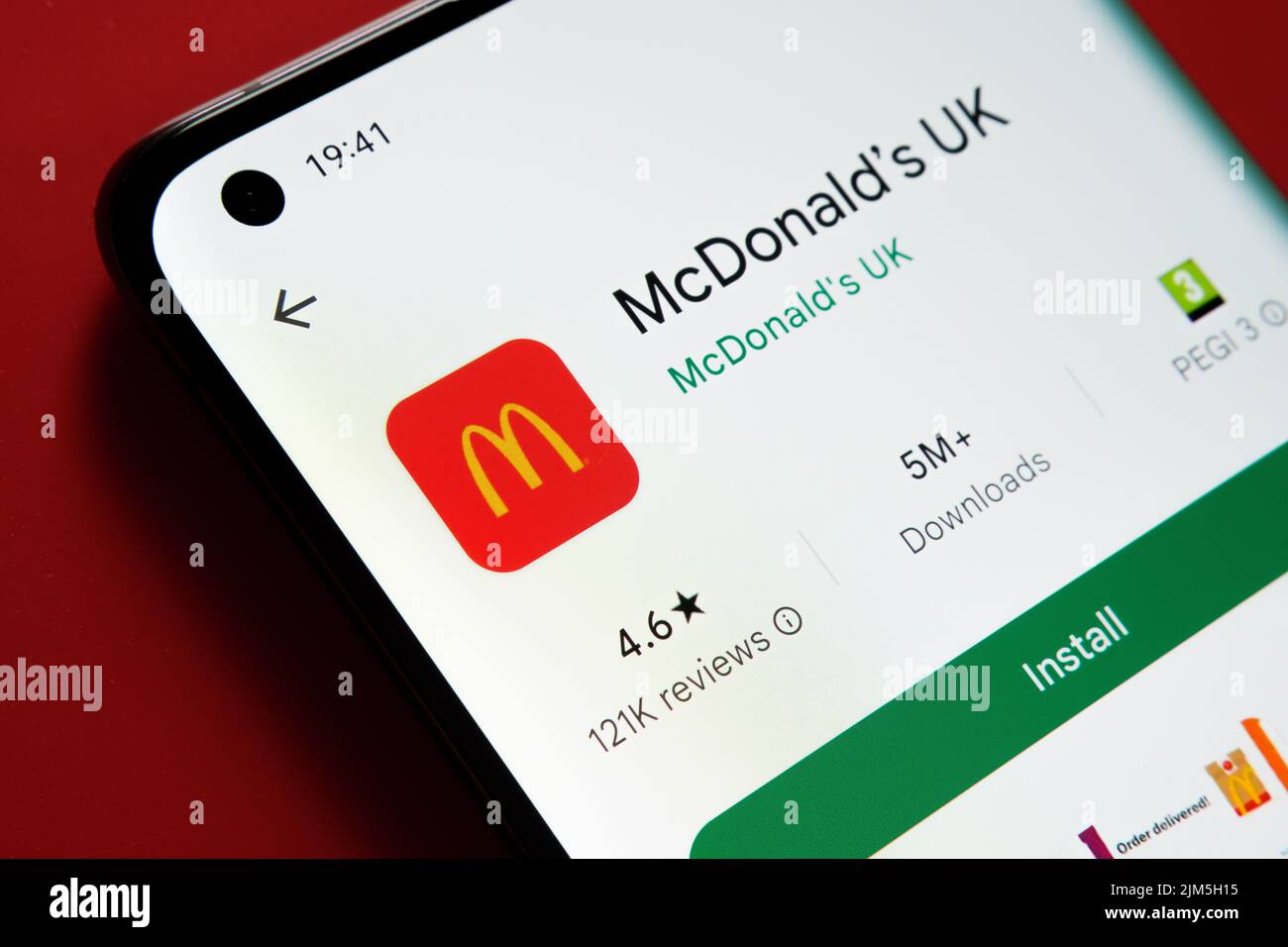 Application McDonald's pour le Royaume-Uni vue dans Google Play Store sur l'écran du smartphone placé sur fond rouge. Gros plan avec mise au point sélective. Stafford, Royaume-Uni Banque D'Images