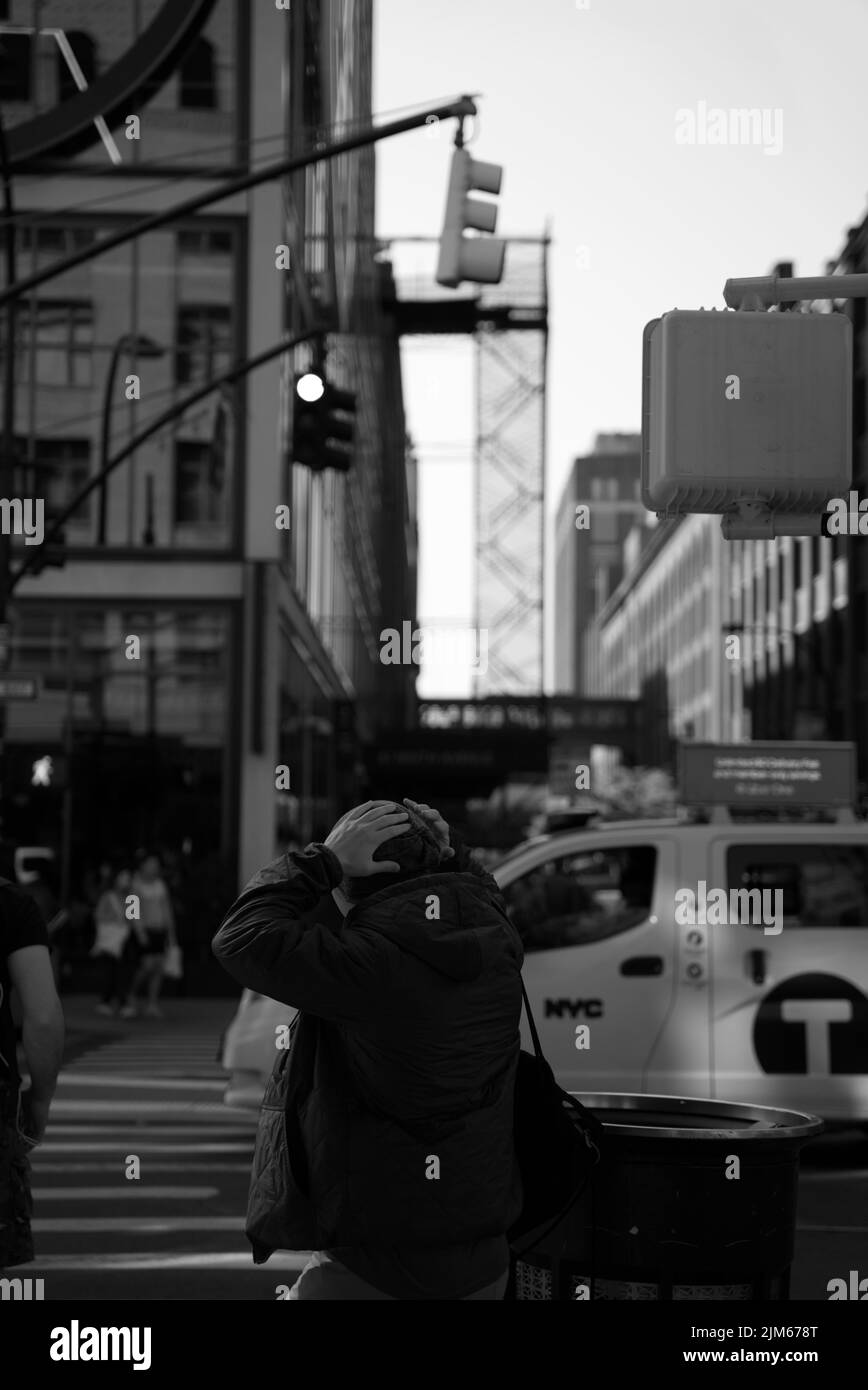 Un gros plan vertical en niveaux de gris d'une personne tenant la tête contre la rue. Times Square, New York. Banque D'Images