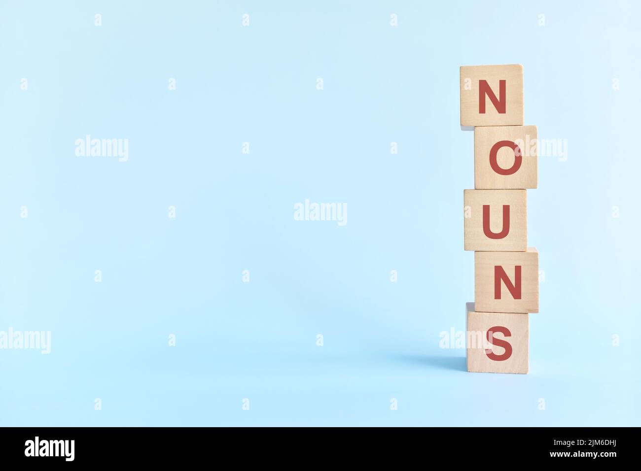 Concept de nom ou de nom dans l'enseignement de la grammaire anglaise. Jeu de mots croisés en bois posé sur fond bleu. Banque D'Images