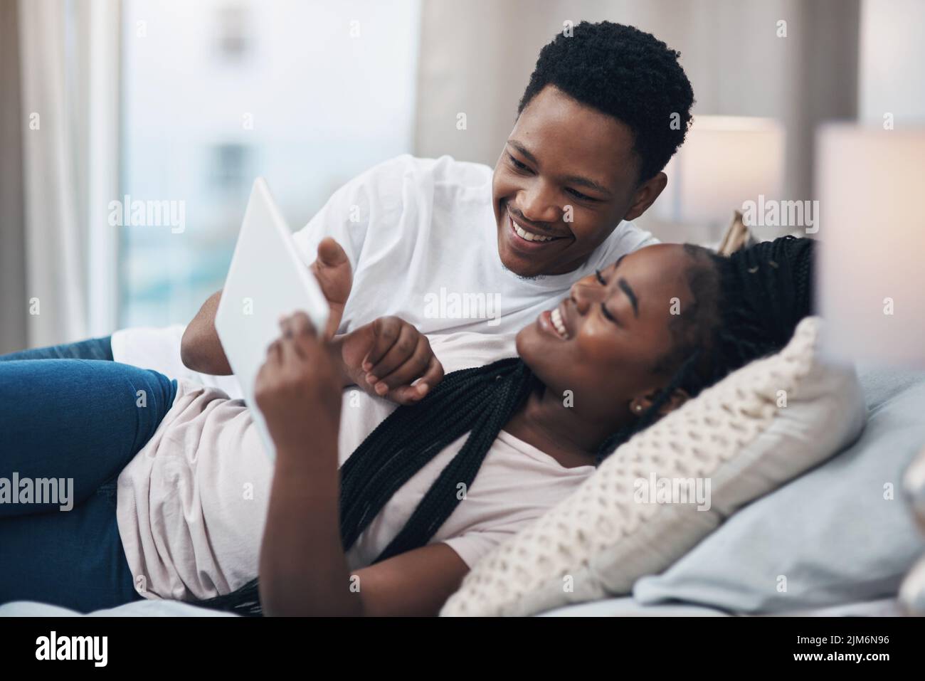 Le plus simple des choses nous rapproche plus que jamais. Un jeune couple utilisant une tablette numérique tout en se relaxant sur son lit à la maison. Banque D'Images