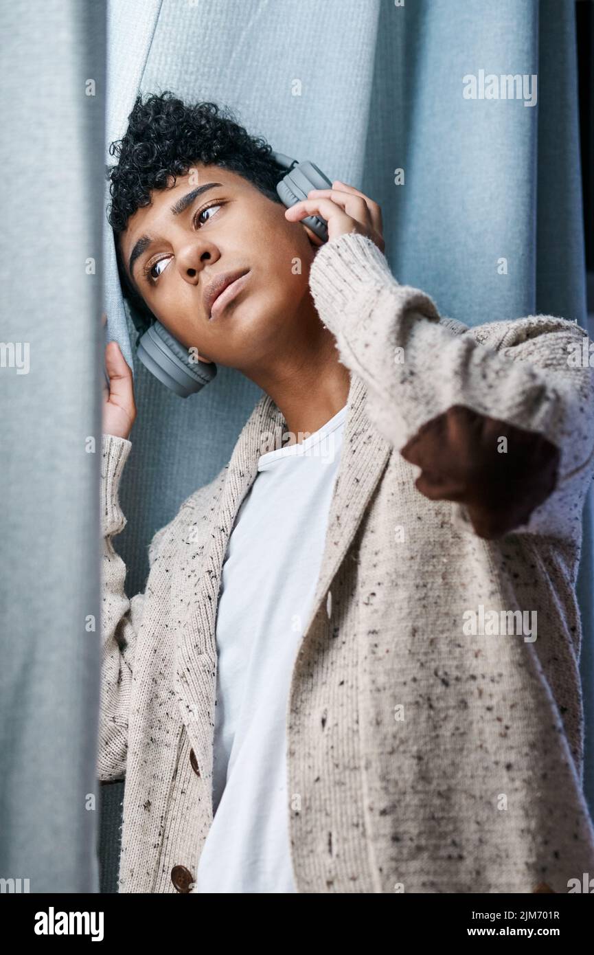 Le verrouillage et les pauses ne se mélangent pas. Un jeune homme utilisant un casque pour écouter de la musique tout en regardant par la fenêtre à la maison. Banque D'Images