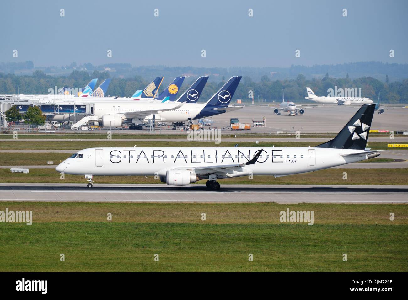 Un avion de Star Alliance décolle devant d'autres avions garés au terminal de l'aéroport de Munich, au départ d'Embraer 190. Banque D'Images