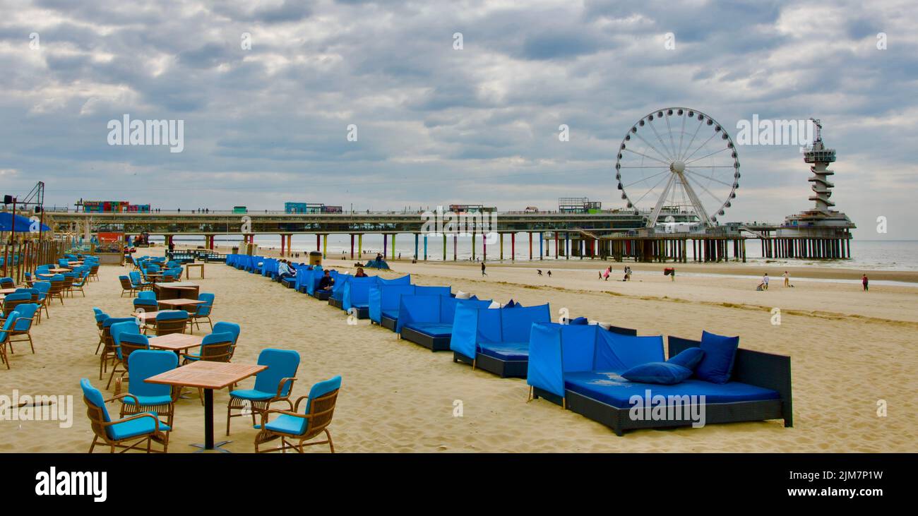 Terrasse de café sur la plage de Scheveningen sans consommateur. Il y a une jetée avec une grande roue de ferris et une tour sur elle en arrière-plan Banque D'Images
