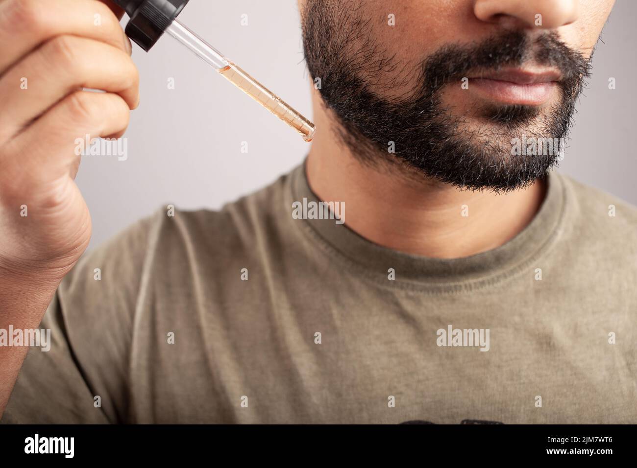 gros plan d'un homme tenant un compte-gouttes rempli de minoxidil qui va s'appliquer à la croissance de la barbe isolée sur fond blanc. Banque D'Images