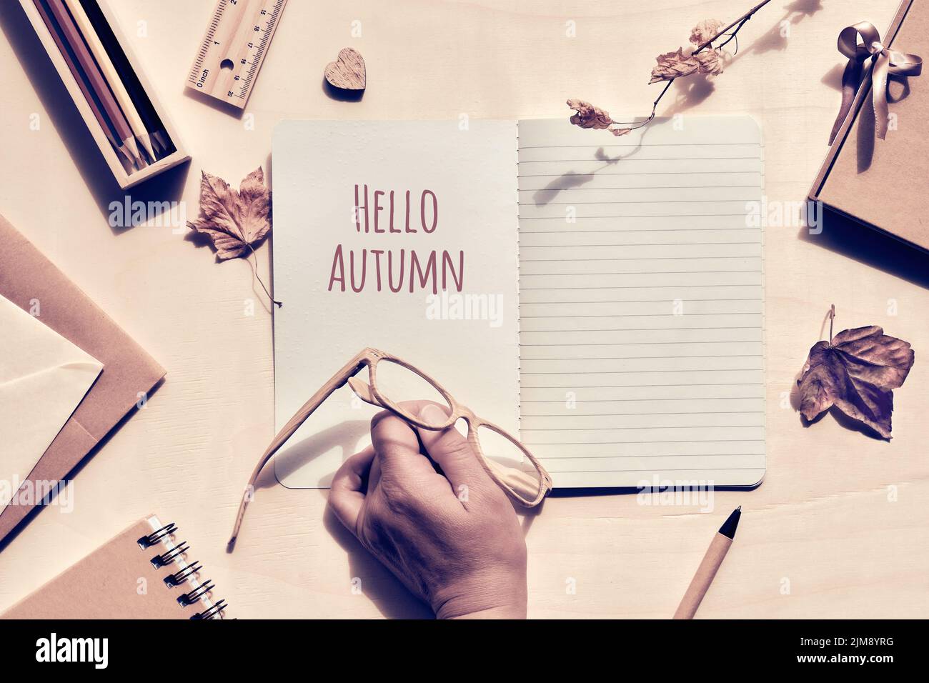 Vieille main avec des verres de lecture en bois, règle, feuilles sèches sur le carnet ouvert avec des mots Hello Autumn. Plat posé sur une table en bois avec fournitures de bureau Banque D'Images