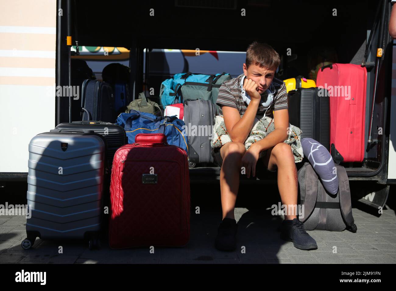 LVIV, UKRAINE - le 4 AOÛT 2022 - Un garçon est assis près des valises dans  le coffre à bagages d'un bus comme une centaine d'enfants de perso déplacés  à l'intérieur du