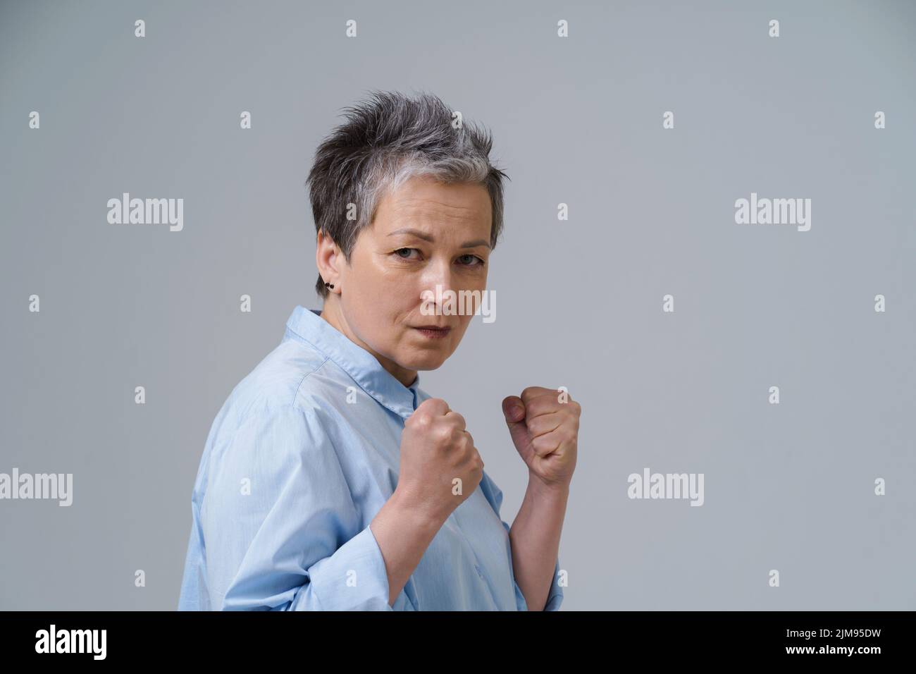 Femme effrayée avec les mains mises dans les poings. Une femme âgée aux cheveux gris se pose comme combattant de boxe sur le point de se tenir debout ou de se protéger. Concept de traite des êtres humains. Femme confiante, forte et agressive. Banque D'Images