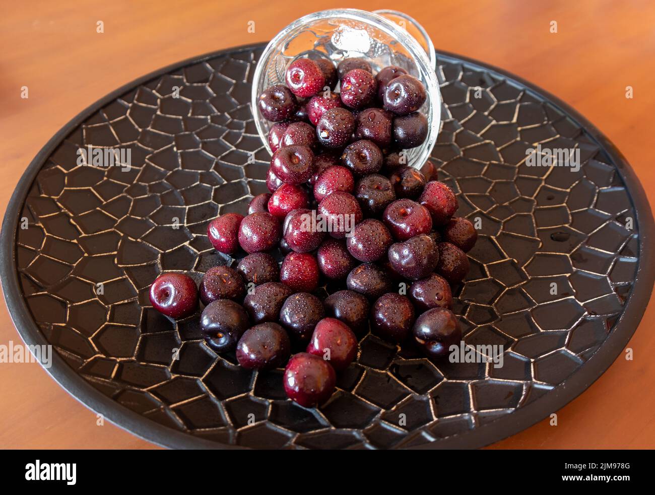 Cerises dans une tasse en verre qui se répande sur un plateau noir Banque D'Images