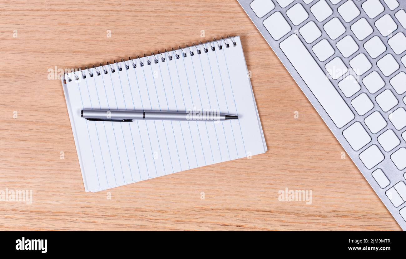 Papier et stylo traditionnels avec clavier sur fond de bureau en chêne rouge Banque D'Images