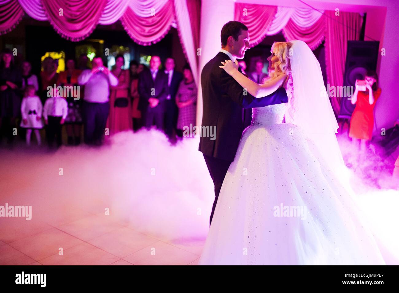 Première danse de mariage étonnant de jeunes mariés en faible lumière rose et la fumée intense Banque D'Images
