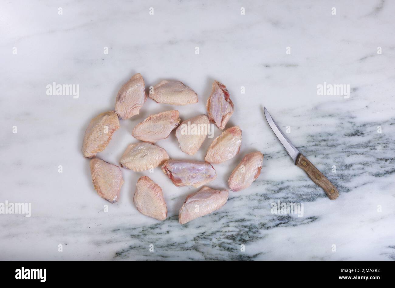 Ailes de poulet frais et couteau de cuisine sur comptoir en pierre de marbre Banque D'Images