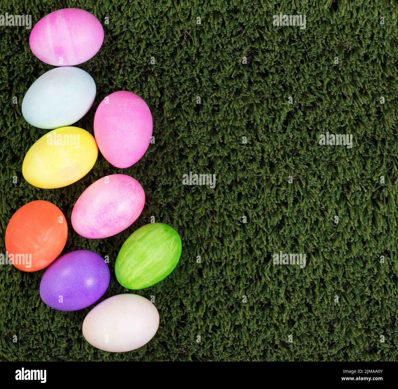 Œufs colorés pour les vacances de Pâques formant la bordure gauche sur l'herbe verte Banque D'Images